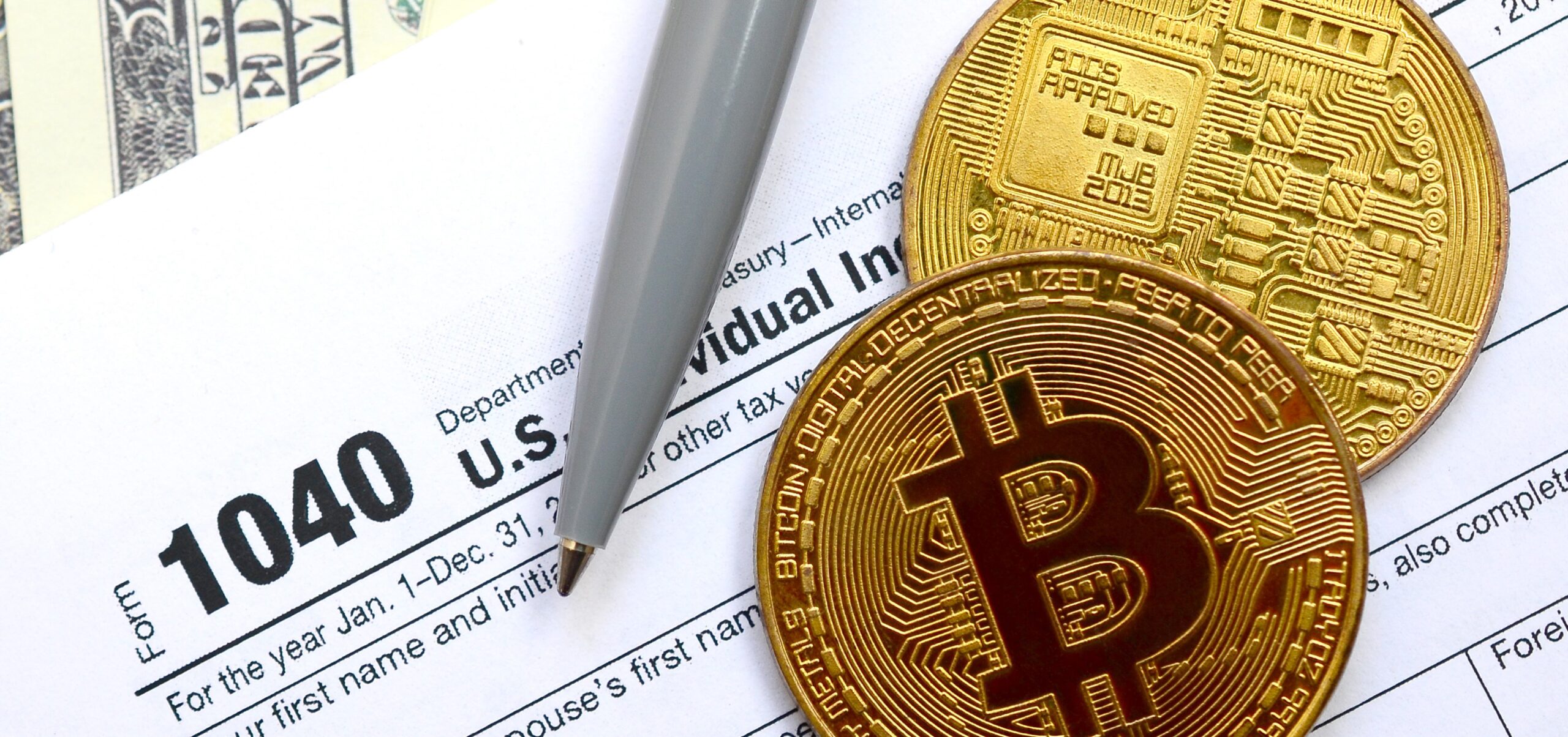 The pen, bitcoins and dollar bills is lies on the tax form 1040 U.S. Individual Income Tax Return. The time to pay taxes